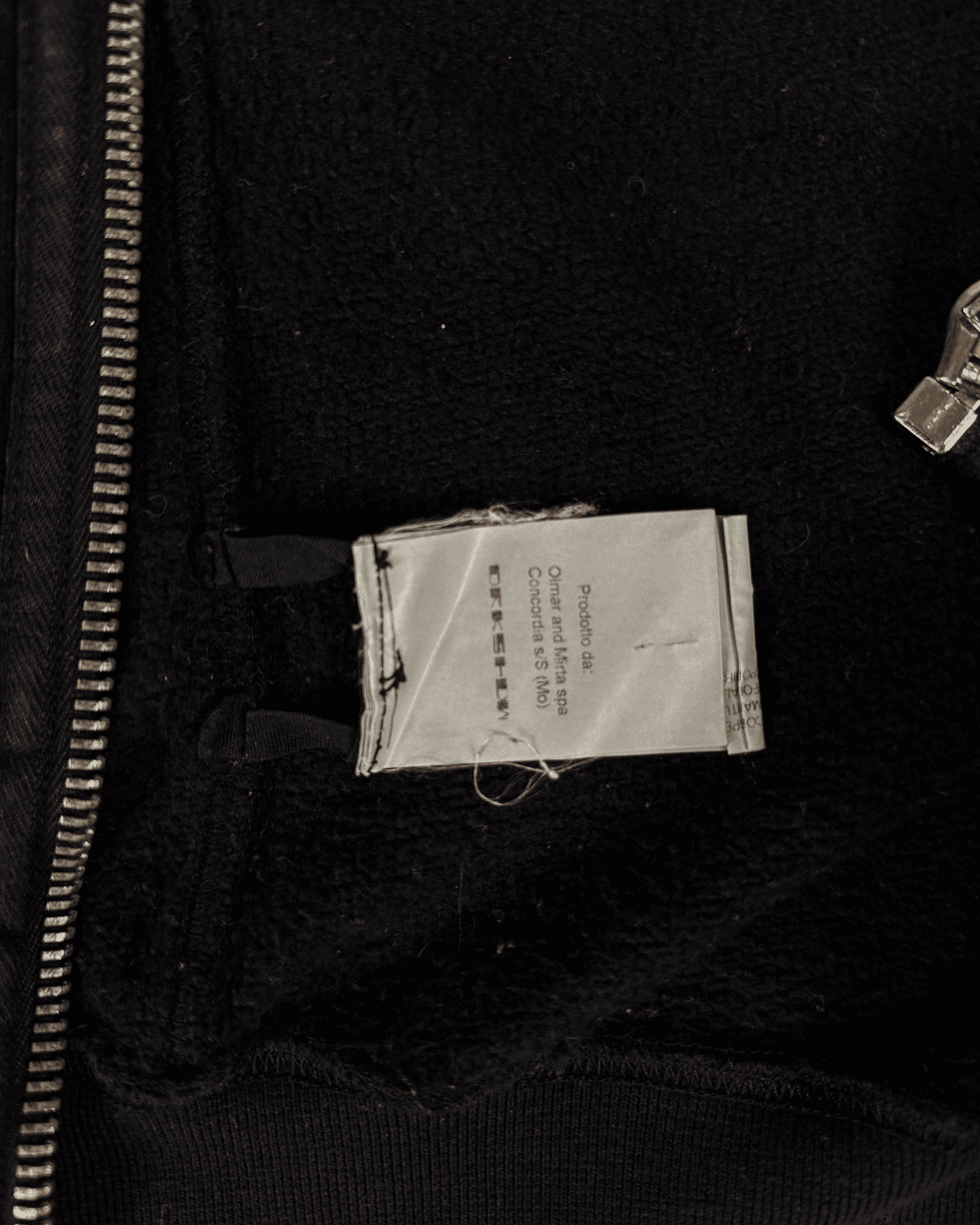Dark hoodie interior showing size/brand label near hem and zipper area
