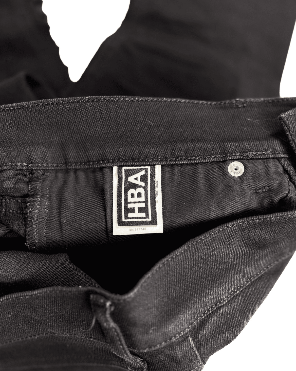 Distressed black denim jeans with HBA label at waistband and metal button